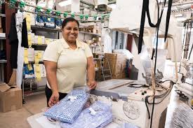 Smiling seamstress standing at ironing station in alteration shop in Tooting with sewing equipment and garments visible in background